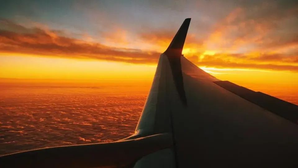 Airplane wing cruising above golden clouds during international flight
